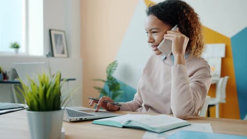 Afro-American Office Worker Talking on Mobile Phone and Using Laptop in Modern Workplace