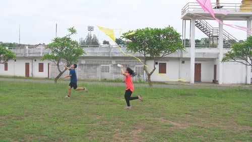 Young Adults Run with Kites on Green Field