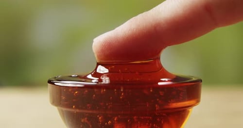 Dipping Finger Into A Bowl Of Sweet Honey A Macro Shot On A Green Background
