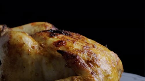 Baked crispy chicken revolving on black background.
