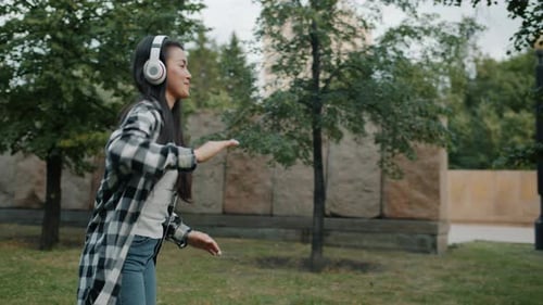 Slow Motion of Asian Lady Dancing Outdoors in City Park Wearing Headphones