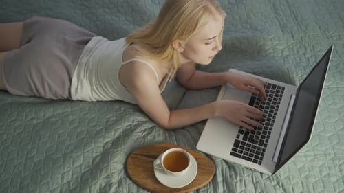 A Young Woman Lies on the Bed and Communicates on a Video Call Via a Laptop