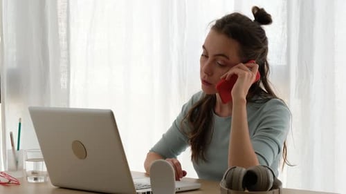 Young Woman Works At Laptop, Talks on Smartphone