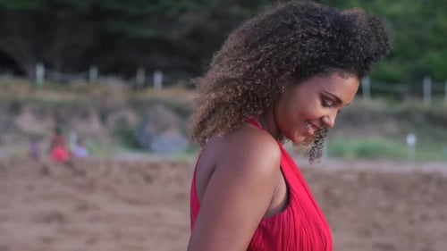 Smiling young woman standing on beach touching her curly hair