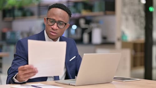 Focused African Businessman Working on Laptop and Documents in Office