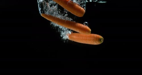 Karotten, Daucus Carota, Gemüse, das vor schwarzem Hintergrund in Wasser gelangt, Zeitlupe 4k