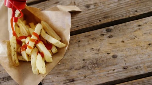 Ketchup being squeezed over french fried chips on tray