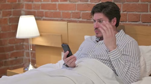 Man Lying in Bed Using Phone
