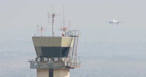 Torre de controle do aeroporto com avião pousando ao fundo
