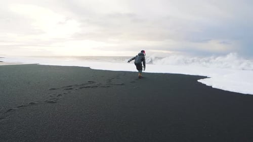 Woman Traveler Running on Volcanic Black Sand Beach in Iceland and Having a Good Time
