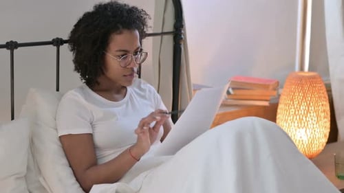 Woman Reading and Writing in Bed with Pen