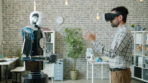 Side View of Developer in Virtual Reality Glasses Moving Hand and Robot Repeating