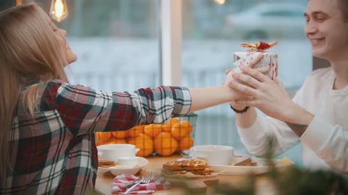 Ein Paar im Café - eine Frau gibt ihrem Freund ein Geschenk - ein Mann küsst sie auf die Wange