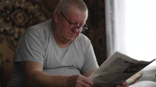 Senior Man Reads Newspaper at Home Indoors