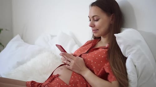 Pregnant Woman Using Cellphone Relaxing on Bed