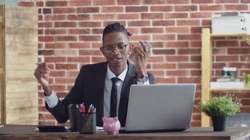 Black Office Worker is Man in Glasses and a Strict Suit Talking on the Phone and Writing with a Pen