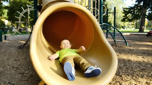 Children Enjoying a Playground Slide on Sunny Day
