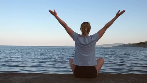 Girl Sitting on the Pier By the Sea and Practices Yoga in the Early Morning