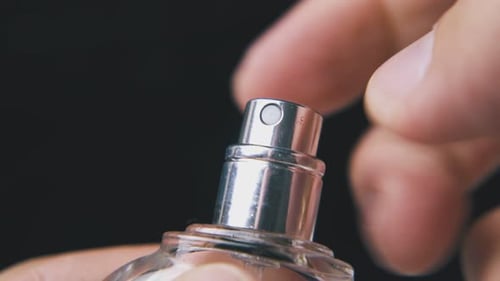 Person sprüht Parfüm aus einer Glasflasche auf dunklem Hintergrund