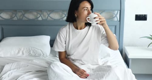Woman having breakfast in bed with coffee or tea cup in bedroom at home