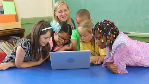 Teacher and students work on laptop computer in school classroom
