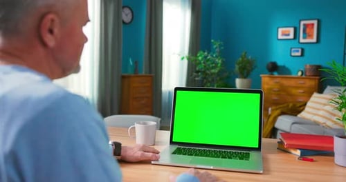 Closeup of a Man Uses Laptop with Green Mockup Screen While Sitting at the Desk