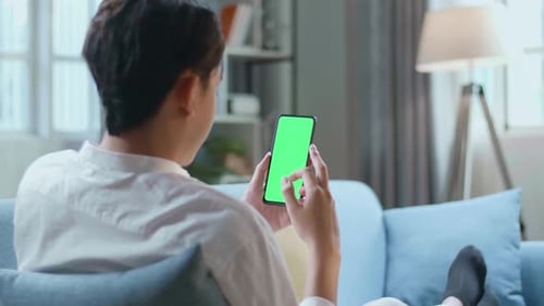 Man Touching Smartphone With Green Screen While Lying On Sofa In The Living Room