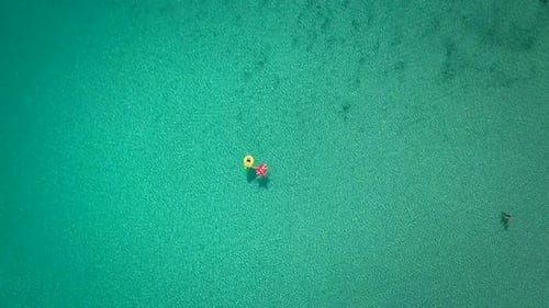 Vista aérea abstrata de duas pessoas flutuando em mar aberto em insufláveis.