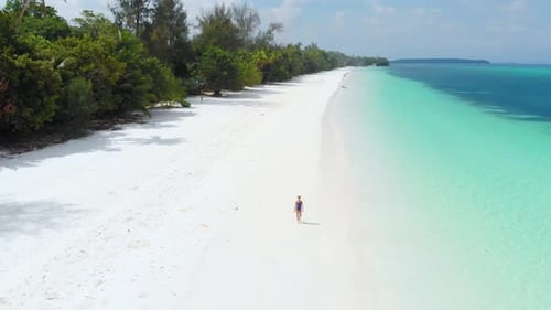 Aerial: woman walking on desert beach, tropical island white sand beach turquoise caribbean sea