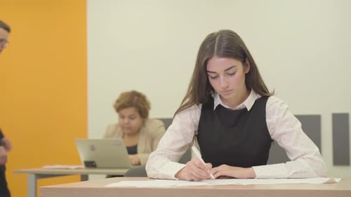 Portrait of a Busy Young Woman in Formal Wear Writing on the Paper in the Foreground in the Office