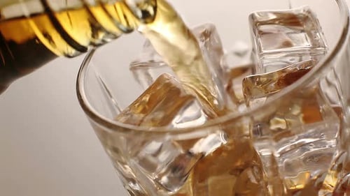 Whiskey pours into a glass filled with ice cubes