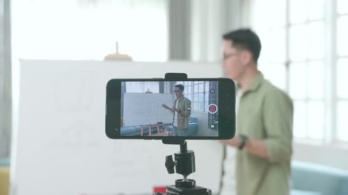 Close Up Of Smartphone Camera Recording Asian Male Teacher With Glasses Teaching Math At Home