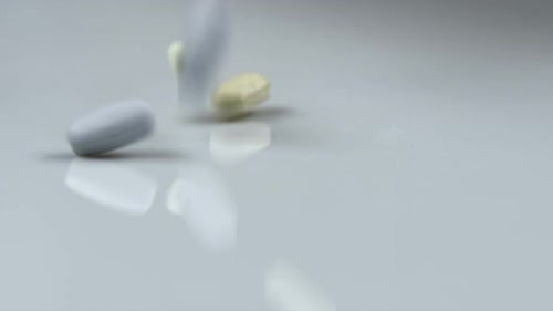 Pills Falling onto White Reflective Surface Close Up