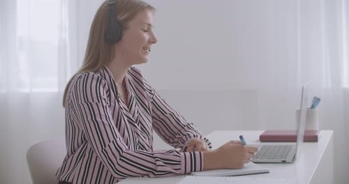 Woman Teleconferencing and Taking Notes at Desk