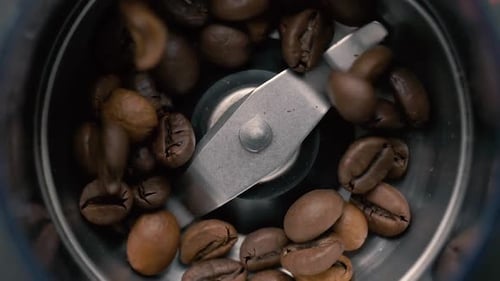 Frisch geröstete Kaffeebohnen werden in eine Mühle aus einem Glas gegossen. Ansicht von oben. Zeitlupe