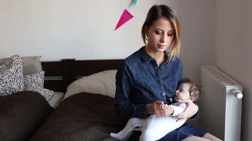 young mother and child on hands sitting on bed at home