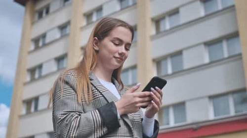 A Girl Walks Through Town and Looks at Her Smartphone