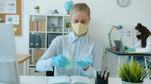 Young Woman in Face Mask and Gloves Washing Hands with Sanitizer in Office