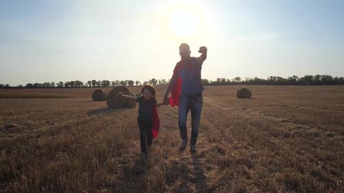 Father and Son As Superheroes Running Across Field
