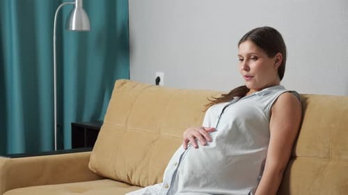 Femme enceinte faisant des exercices de respiration éprouvant des contractions alors qu'elle est assise sur le canapé