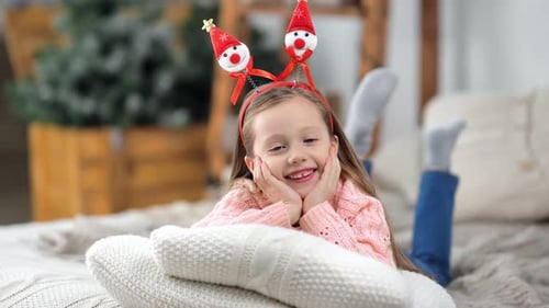Smiling Girl in Christmas Headband Lying on Pillows