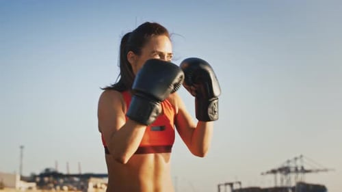 Young Hardy Female in Leather Boxing Gloves and Sportswear is Boxing While Training Near the City
