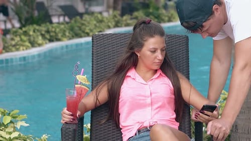 Woman Looks at Phone with Drink by Pool