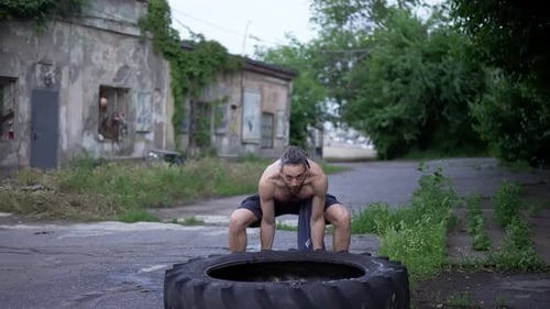 Shirtless Man Pushes Raises Large Wheel From Tractor Outdoors