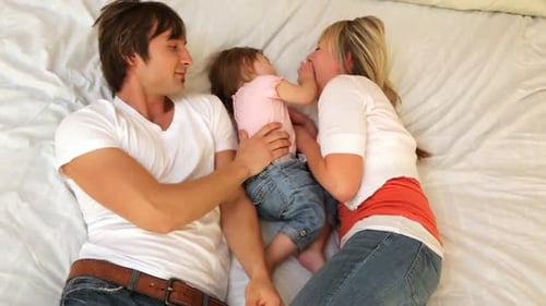 Loving Parents Playfully Tickle Young Child on Bed