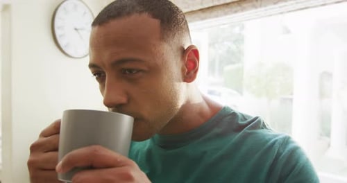 Young Man Drinking from Mug in Kitchen