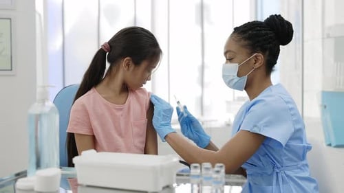 Crop View of Female Nurse in Protective Mask Vaccinating Little Girl Into Shoulder and Giving High