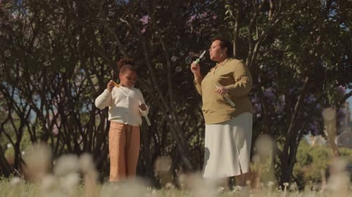 Mother and Daughter Blowing Soap Bubbles in Park