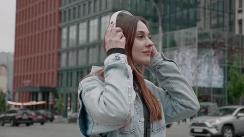 Woman Listens to Music in City with Headphones