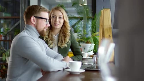 Blonde Woman Discussing Project on Laptop with Male Colleague in Cafe
